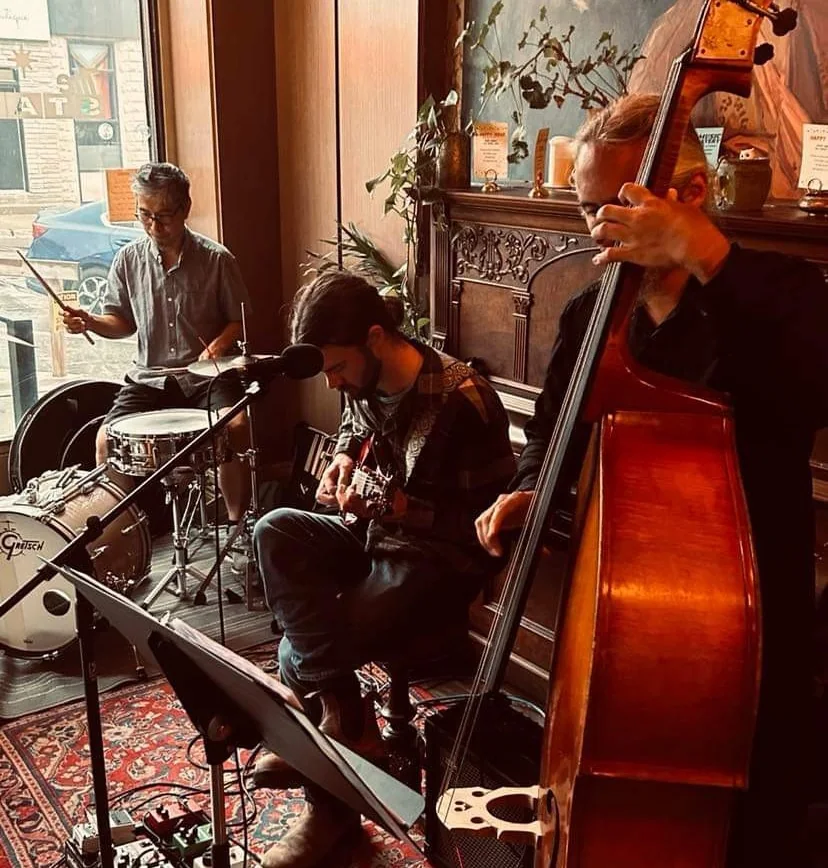 The trio mid-set in the corner of the Starlight: Gop at the drums, Luke on guitar, Hoai on upright bass, a music stand and a red rug in the foreground.
