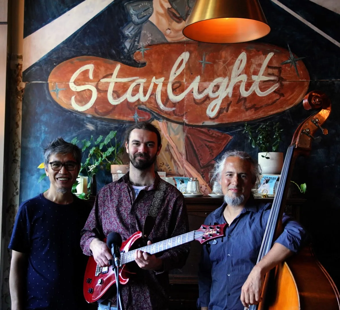 The three of them under the painted Starlight sign: Gop, Luke with the red guitar, Hoai with the upright.